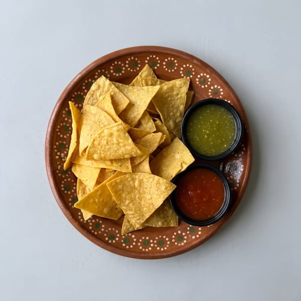 Tortilla chips on a decorative brown plate with small bowls of red and green salsa.